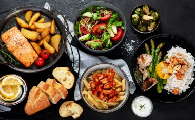 Bir dizi ana yemek. Farklı sağlıklı ana yemekler, et ve balık yemekleri, makarna, salatalar, soslar, arka planda ekmek ve sebzeler. Üst görünüm.