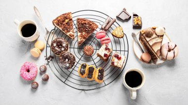 Arka planda çeşitli kurabiyeler, çörekler, kekler ve kahve fincanları olan masa. Üst görünüm.