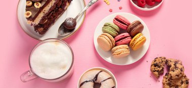 Çeşitli kurabiyeler, çörekler, kekler, peynirli kekler ve pembe arka planda kahve fincanları. Lezzetli tatlı masası. Üst manzara, düz yatak, panorama, pankart