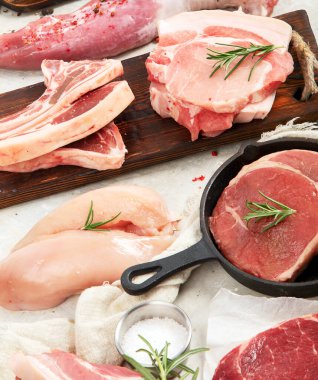 Çeşitli taze et türleri: gri arka planda domuz eti, sığır eti ve tavuk. Üst görünüm.