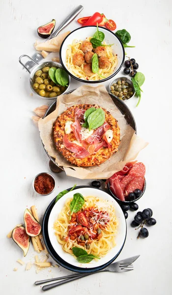 プレートとボード上のイタリア料理の完全なテーブル パスタ ミートボール サラミ パルメザンチーズ オリーブ 白い背景にパンスティック トップ表示 — ストック写真