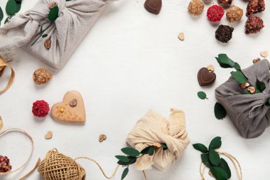 Zero waste Valentine's Day concept. Eco-friendly gift cloth wrapping in Furoshiki style, homemade sweets and cookies as gift ideas on white background. Top view or flat lay.