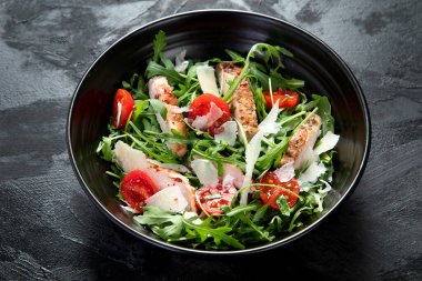 Chicken breast and fresh vegetable salad of lettuce, arugula, spinach, parmesan and tomatoes in dark plate. Healthy mediterranean dish. Keto Diet eating. 