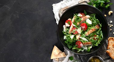 Chicken breast and fresh vegetable salad of lettuce, arugula, spinach, parmesan and tomatoes in dark plate. Healthy mediterranean dish. Keto Diet eating. Top view, copy space