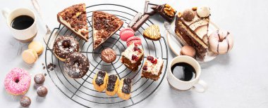 Table with various cookies, donuts, cakes and coffe cups on light backround. Top view. Panorama, banner.