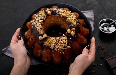 Bundt chocolate cake decorated with melted chocolate, nuts  and sprinkles on plate  on black background. Holiday concept. Top view with copy space