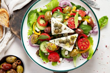 Greek salad of fresh cucumber, tomato, sweet pepper, lettuce, red onion, feta cheese and olives with olive oil on a white background. Healthy food, top view. 