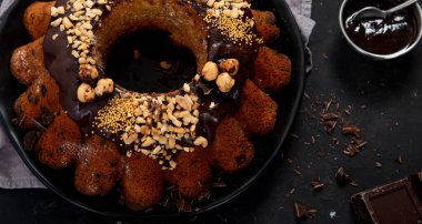 Bundt chocolate cake decorated with melted chocolate, nuts  and sprinkles on plate  on black background. Holiday concept. Top view with copy space