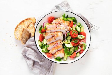 Grilled chicken breast, fillet and fresh vegetable salad of lettuce, arugula, spinach, cucumber and tomato on a white background. Healthy lunch menu. Diet food. Top view.