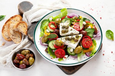 Greek salad of fresh cucumber, tomato, sweet pepper, lettuce, red onion, feta cheese and olives with olive oil on a white background. Healthy food, top view. 