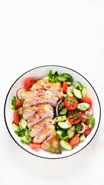 Grilled chicken breast, fillet and fresh vegetable salad of lettuce, arugula, spinach, cucumber and tomato on a white background. Healthy lunch menu. Diet food. Top view.