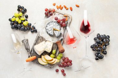 Pink and red wine served with cheeses, nuts, grapes and glasses of wine. Delicious food wine snacks assorted served on boards. Flat lay on a white background.