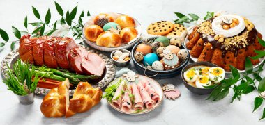 Classic Easter ham dinner. Top view table scene on a white background. Ham, eggs, hot cross buns, carrot, cake and vegetables.