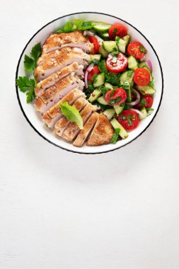 Grilled chicken breast, fillet and fresh vegetable salad of lettuce, arugula, spinach, cucumber and tomato on a white background. Healthy lunch menu. Diet food. Top view.