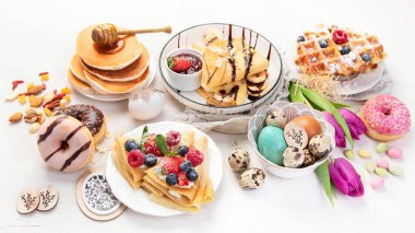 Easter sweet dessert table. Pancakes, crepes, waffles and donuts  with fresh berries, nuts and topping.   Easter traditional natural colorful eggs. 