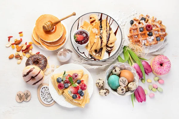 Easter sweet dessert table. Pancakes, crepes, waffles and donuts  with fresh berries, nuts and topping.   Easter traditional natural colorful eggs. Top view, flat lay