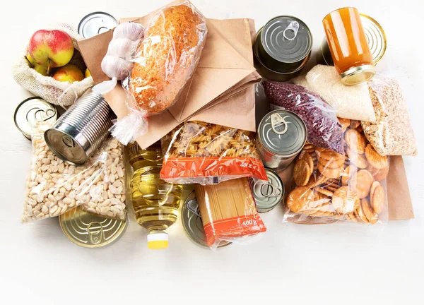 Food donations with pasta, rice, oil, peanut butter, canned food, jam and other  on light background, top view. Food donations or delivery concept.
