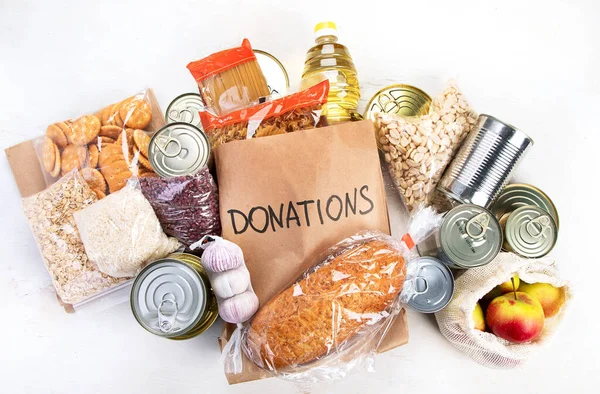 Food donations with pasta, rice, oil, peanut butter, canned food, jam and other  on light background, top view. Food donations or delivery concept.