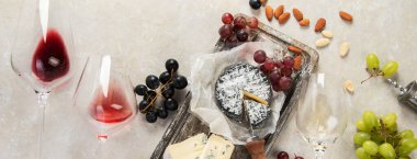Pink and red wine served with cheeses, nuts, grapes and glasses of wine. Delicious food wine snacks assorted served on boards. Flat lay on a white background. Panorama.