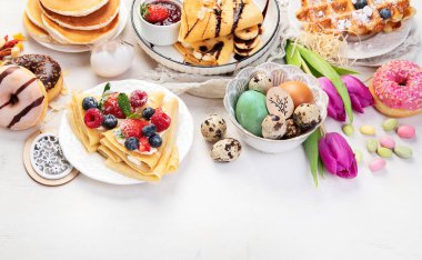 Easter sweet dessert table. Pancakes, crepes, waffles and donuts  with fresh berries, nuts and topping.   Easter traditional natural colorful eggs. 