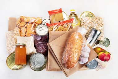 Food donations with pasta, rice, oil, peanut butter, canned food, jam and other  on light background, top view. Food donations or delivery concept.