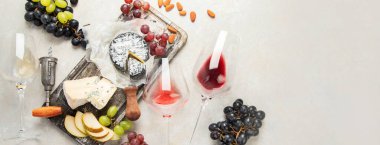 Pink and red wine served with cheeses, nuts, grapes and glasses of wine. Delicious food wine snacks assorted served on boards. Flat lay on a white background. Panorama with copy space.