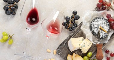 Pink and red wine served with cheeses, nuts, grapes and glasses of wine. Delicious food wine snacks assorted served on boards. Flat lay on a white background. Panorama.