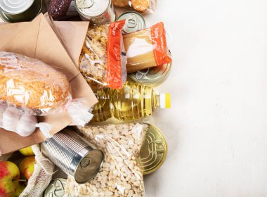 Food donations with pasta, rice, oil, peanut butter, canned food, jam and other  on light background, top view with copy space. Food donations or delivery concept.