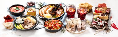 Typical spanish tapas concept. Concept include jamon, chorizo sausage, brushettas, bowl with olives, shrimp, pan with paella, cheese, sangria, churros on a white background. Top view.