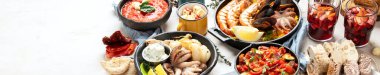 Typical spanish tapas concept. Concept include jamon, chorizo sausage, brushettas, bowl with olives, shrimp, pan with paella, cheese, sangria, churros on a white background. Top view. Panorama with copy space.