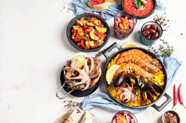 Typical spanish tapas concept. Concept include jamon, chorizo sausage, brushettas, bowl with olives, shrimp, pan with paella, cheese, sangria, churros on a white background. Top view. Copy space.
