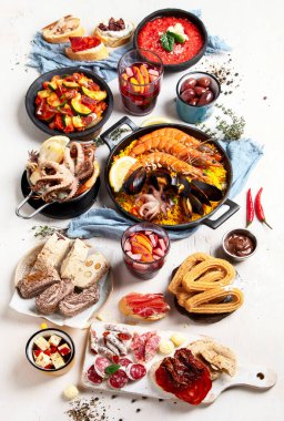 Typical spanish tapas concept. Concept include jamon, chorizo sausage, brushettas, bowl with olives, shrimp, pan with paella, cheese, sangria, churros on a white background. Top view.