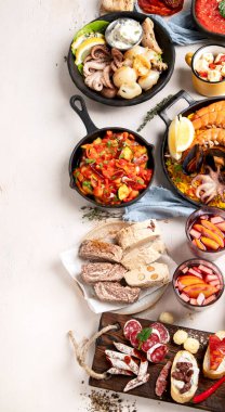 Typical spanish tapas concept. Concept include jamon, chorizo sausage, brushettas, bowl with olives, shrimp, pan with paella, cheese, sangria, churros on a white background. Top view. Copy space.
