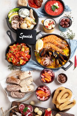 Typical spanish tapas concept. Concept include jamon, chorizo sausage, brushettas, bowl with olives, shrimp, pan with paella, cheese, sangria, churros on a white background. Top view.
