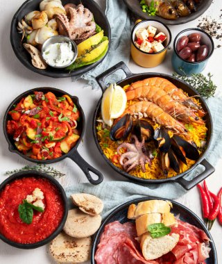 Typical spanish tapas concept. Concept include jamon, chorizo sausage, brushettas, bowl with olives, shrimp, pan with paella, cheese, sangria, churros on a white background. Top view.