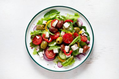 Greek salad of fresh cucumber, tomato, sweet pepper, lettuce, red onion, feta cheese and olives with olive oil on a white background. Healthy food, top view. 