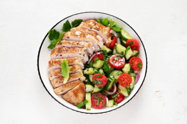 Grilled chicken breast, fillet and fresh vegetable salad of lettuce, arugula, spinach, cucumber and tomato on a white background. Healthy lunch menu. Diet food. Top view.