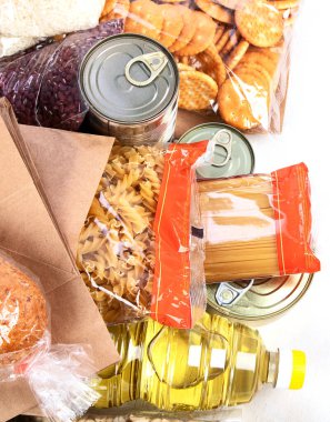 Food donations with pasta, rice, oil, peanut butter, canned food, jam and other  on light background, top view. Food donations or delivery concept.