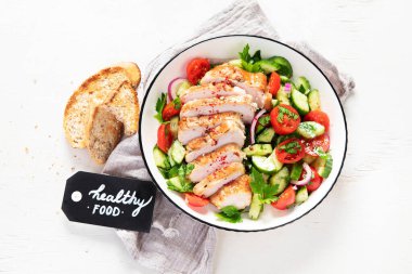Grilled chicken breast, fillet and fresh vegetable salad of lettuce, arugula, spinach, cucumber and tomato on a white background. Healthy lunch menu. Diet food. Top view.