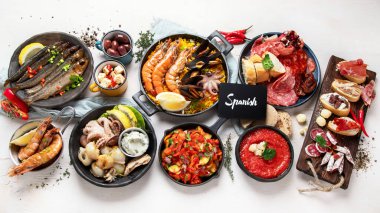 Typical spanish tapas concept. Concept include jamon, chorizo sausage, brushettas, bowl with olives, shrimp, pan with paella, cheese, sangria, churros on a white background. Top view.