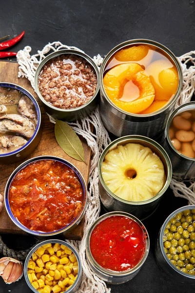 Various canned vegetables, meat, fish and fruits in tin cans. On a dark background. Top view.