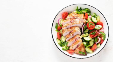 Grilled chicken breast, fillet and fresh vegetable salad of lettuce, arugula, spinach, cucumber and tomato on a white background. Healthy lunch menu. Diet food. Top view. Panorama with copy space.