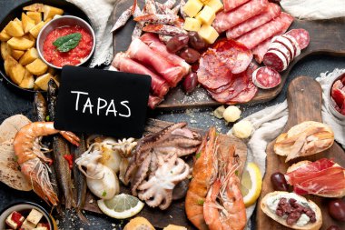 Typical spanish tapas with jamon slices, chorizo, salami,  olives,  potatoes snack Patatas bravas, seafoods on dark table. Traditional spanish food. Top view. 