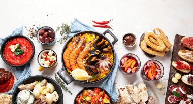 Typical spanish tapas concept. Concept include jamon, chorizo sausage, brushettas, bowl with olives, shrimp, pan with paella, cheese, sangria, churros on a white background. Top view. Panorama with copy space.