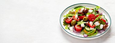 Greek salad of fresh cucumber, tomato, sweet pepper, lettuce, red onion, feta cheese and olives with olive oil on a white background. Healthy food, top view. Panorama with copy space.