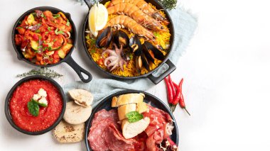 Typical spanish tapas concept. Concept include jamon, chorizo sausage, brushettas, bowl with olives, shrimp, pan with paella, cheese, sangria, churros on a white background. Top view. Copy space.