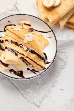 Muzlu krep, doğranmış badem ve beyaz tabakta çikolata sosu, beyaz arka planda masa üstü manzarası. Lezzetli Fransız krepleri..