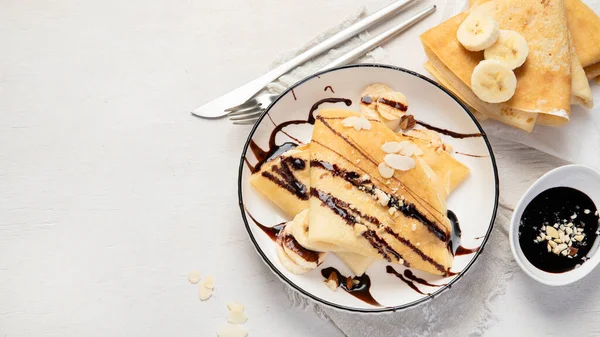 ホワイトプレートにバナナ 刻んだアーモンドとチョコレートソース 白い背景のテーブルトップビューでクレープ おいしいフランス風のクレープ — ストック写真