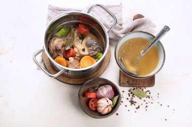 Etli et çorbası yavaş yavaş sebzelerle pişiriliyor: havuç, soğan, sarımsak ve baharatlar beyaz bir arka planda, malzemelerle servis ediliyor..