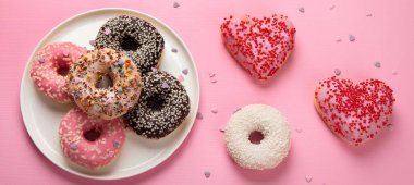 Çikolatalı donut, marşmelov ve pembe arka planda şeker serpiştirme, üst manzara. Renkli karnaval ya da doğum günü partisi kartı. Ulusal Çörek Günü 'nüz kutlu olsun. Panorama.